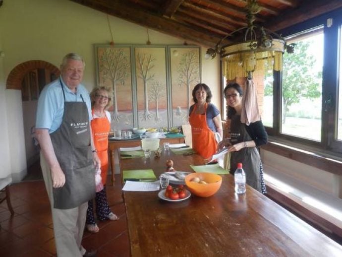 Cooking guests with aprons in Tuscany kitchen during cookery lesson.