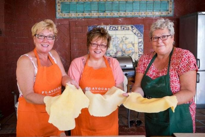 Three ladies in aprons smiling and holding pizza dough