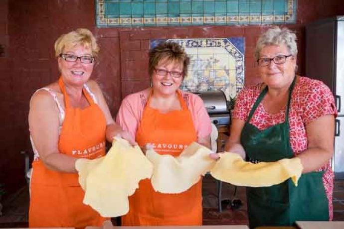 Three guests in apron preparing pizza dough.