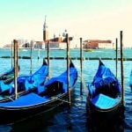 Venice's infamous gondolas floating in the water with the city of Venice in the background