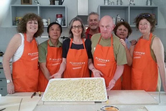Guests with aprons standing in kitchen presenting tray of homemade orechiette.
