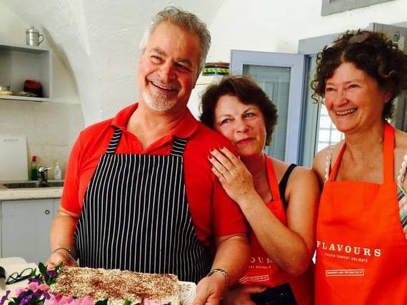 Italian chef and cookery guests presenting cake. Italian chef Antonio and 2 female cookery guests in apron presenting freshly made cake in rustic kitchen.