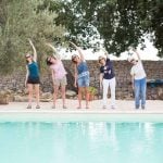 Five women standing at pool and doing Pilates pose.