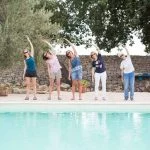 Five women standing at pool and doing Pilates pose.