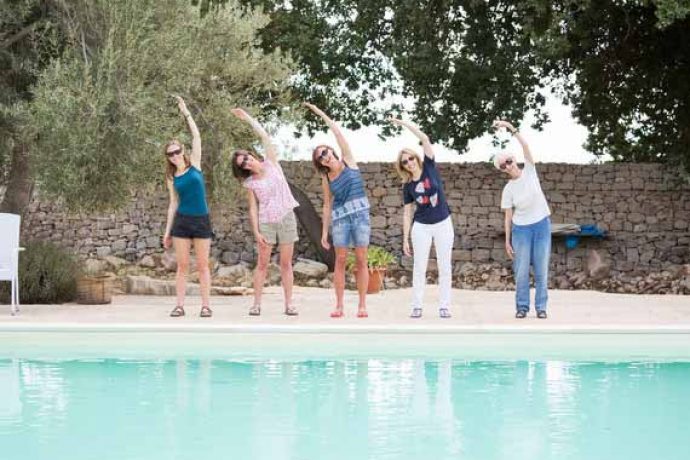 Five women standing at pool and doing Pilates pose.