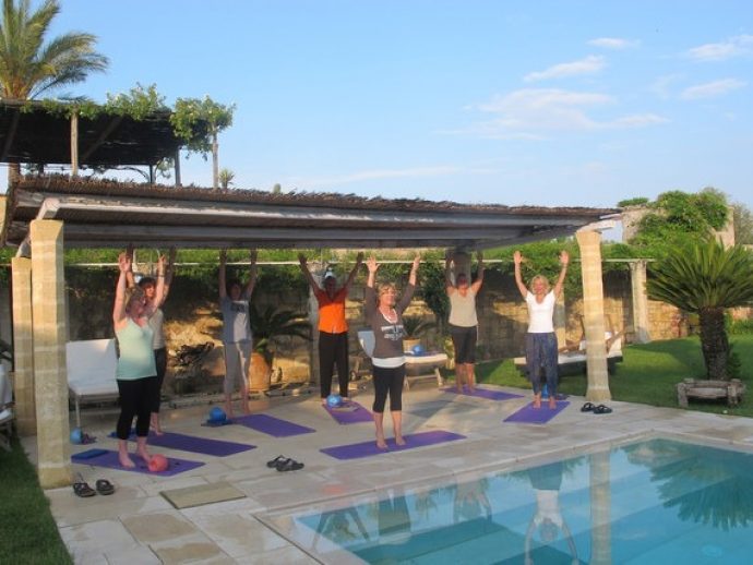 Pilates group with hands up high by the pool in Puglia