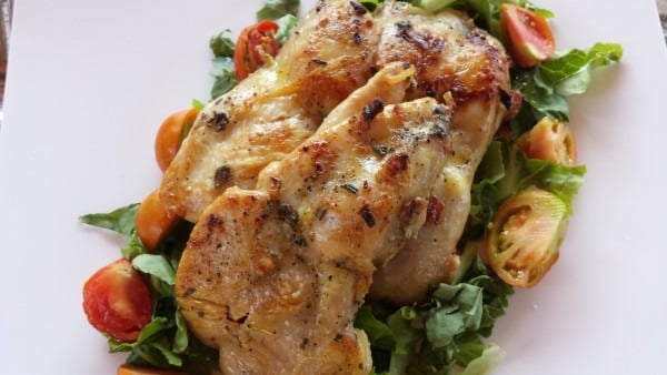 A plate of marinated chicken pieces on a bed of tomato and salad leaves: Pollo Dorato