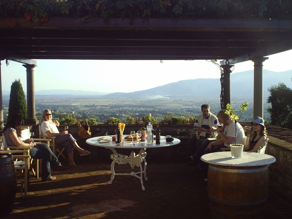 Group of Italian holiday guests around a white table with drinks overlooking an Italian mountain panorama