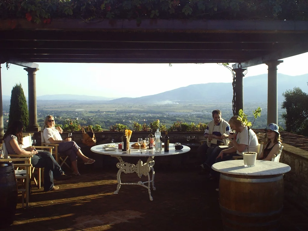 Group of Italian holiday guests around a white table with drinks overlooking an Italian mountain panorama