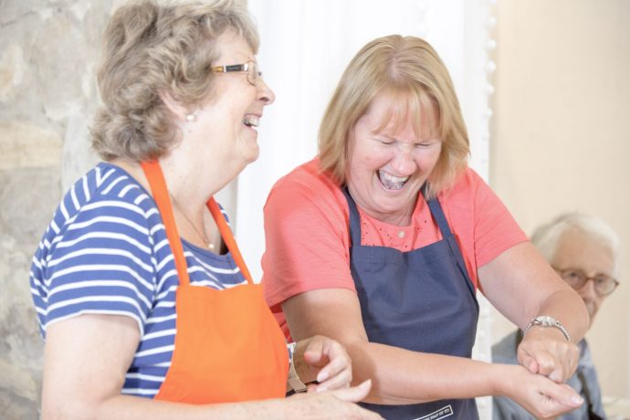 Two mature women laughing while cooking