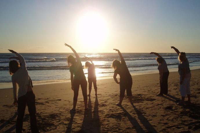 Group practicing Pilates on the beach at sunset