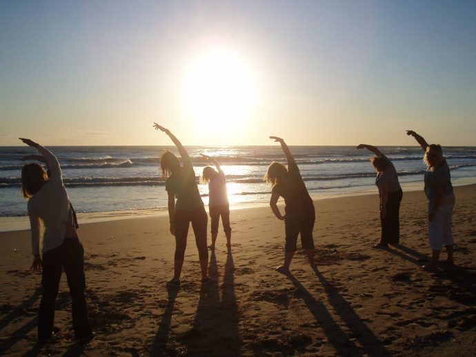 Group practicing Pilates on the beach at sunset