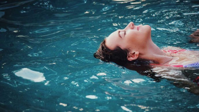 Our favourite wellness podcasts for this year - girl relaxing in a pool