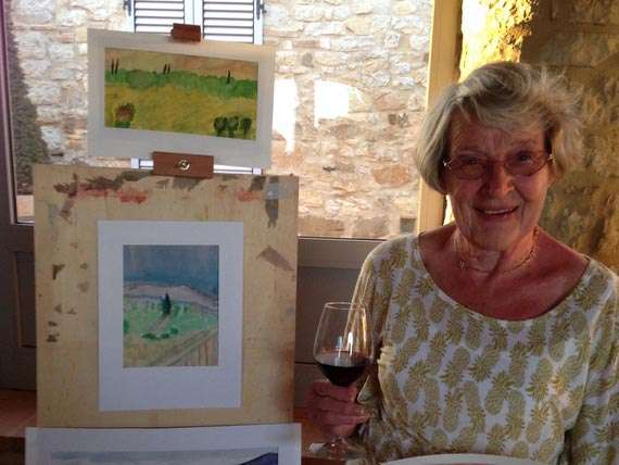 Painting holiday guest with painting. Mature lady with glass of wine next to easel and watercolour painting.